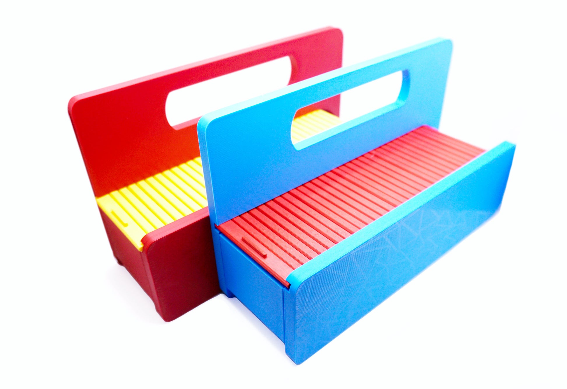 The Garage Door style deck box for Beyblade X in Sky Blue for the base with a red door and tray next to another one in red for the base and yellow for the door with all against a white background