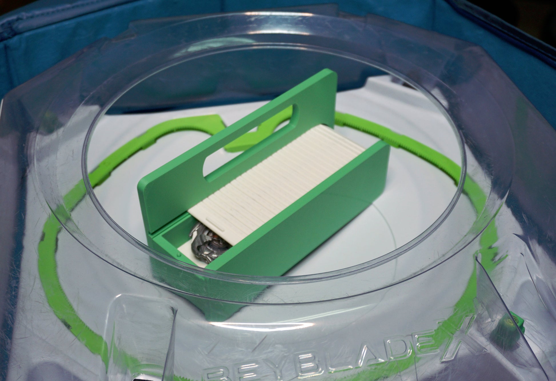 The Garage Door style deck box for Beyblade X in green for the base with a white door and tray. With Weiss Tiger, Meteor Dragoon, Dran Blast inside the case. With the deck box sitting inside a Takara Tomy stadium with Level Locks from Momo's Models