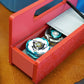 A red base with silver door and tray Garage Door style deckbox sitting on a wooden table. Next to it is a Takara Tomy stadium in a case and a red ripcord launcher with red handle and cherry red slip grip attachment. Inside the deck box is Emperor Blast and Wolf Hunt