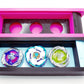 The Beyblade X Garage Door style deckbox from Momo's Models shown in black with glacier color scheme and a hot pink and black color scheme. Inside the black/glacier deckbox is Shark Scale, Pegasus Blast, and Hover Wyvern (Pringle) beyblades. With everything against a white background
