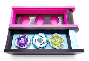 The Beyblade X Garage Door style deckbox from Momo's Models shown in black with glacier color scheme and a hot pink and black color scheme. Inside the black/glacier deckbox is Shark Scale, Pegasus Blast, and Hover Wyvern (Pringle) beyblades. With everything against a white background