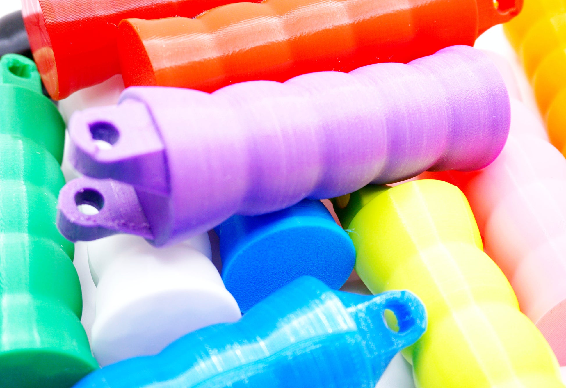 A pile of the Beyblade X Full Grip Handles, colors shown in the pile are green, purple, white, blue, sky blue, lime, red, and orange