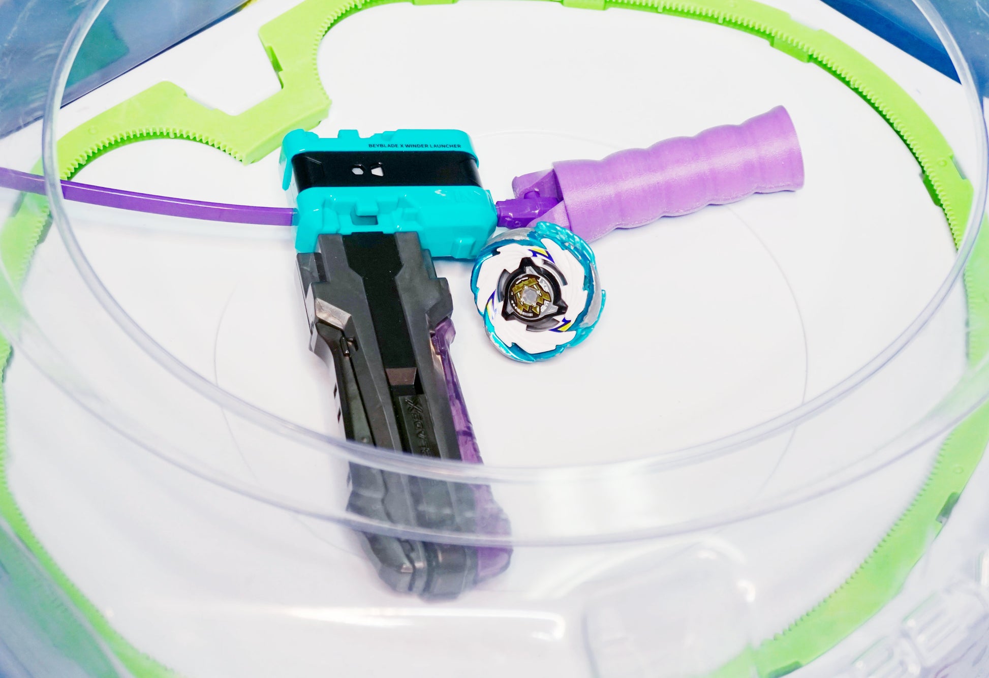 The Beyblade X Full Grip Handle in purple on the teal ripcord launcher with grey handle. Next to a Pegasus Blast CX beyblade in the Takara Tomy Stadium