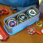 A top down view of the Beyblade X Deckbox from Momo's Models shown in the Grey and Sky Blue color combination. With a red ripcord launcher and slip grip next to it, along with a few beyblade parts. All on a wooden table next to a Takara Tomy stadium