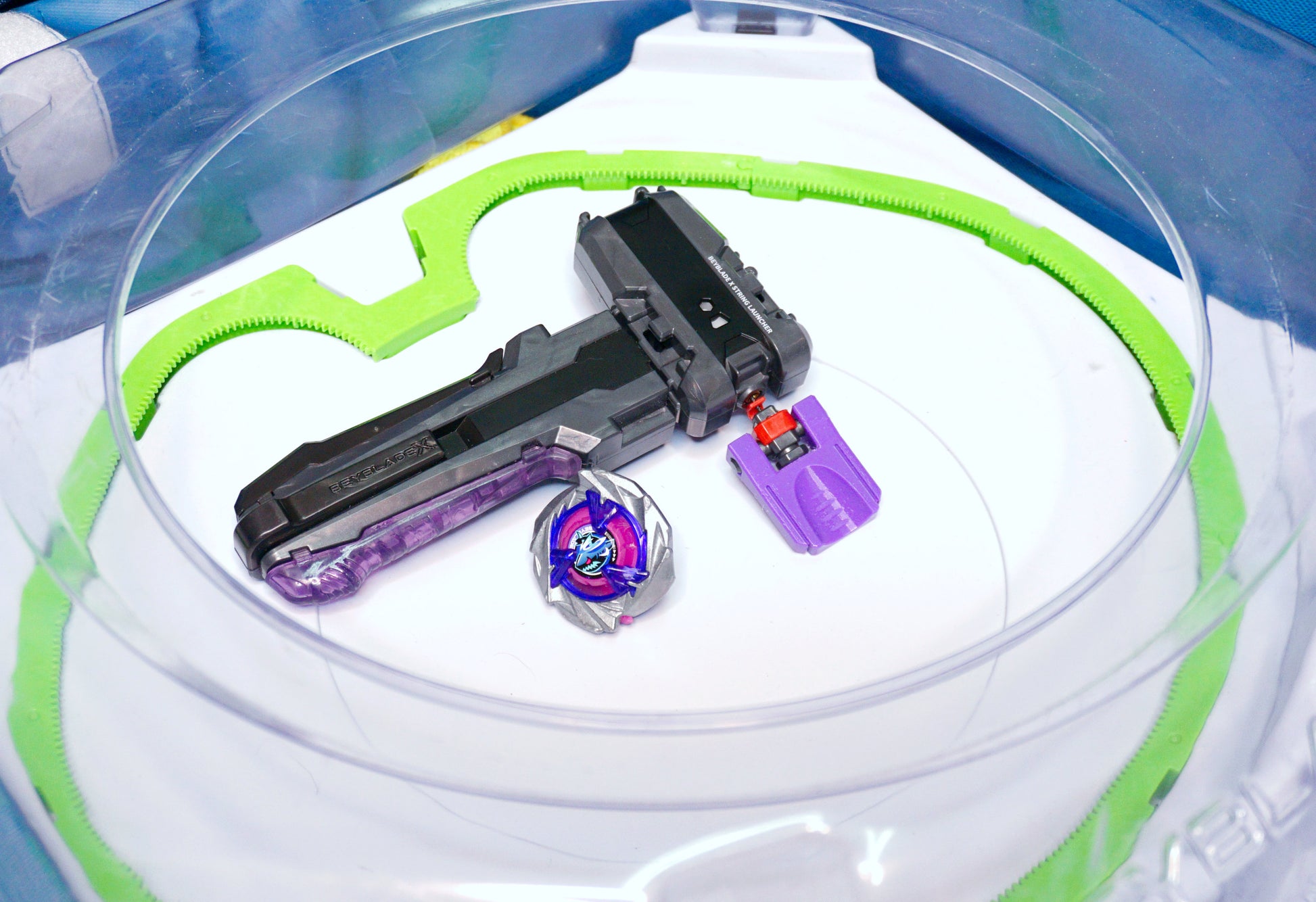 The purple Thumb Tab on the black string launcher with the grey handle grip. Sitting in the beyblade stadium with the Shark Scale
