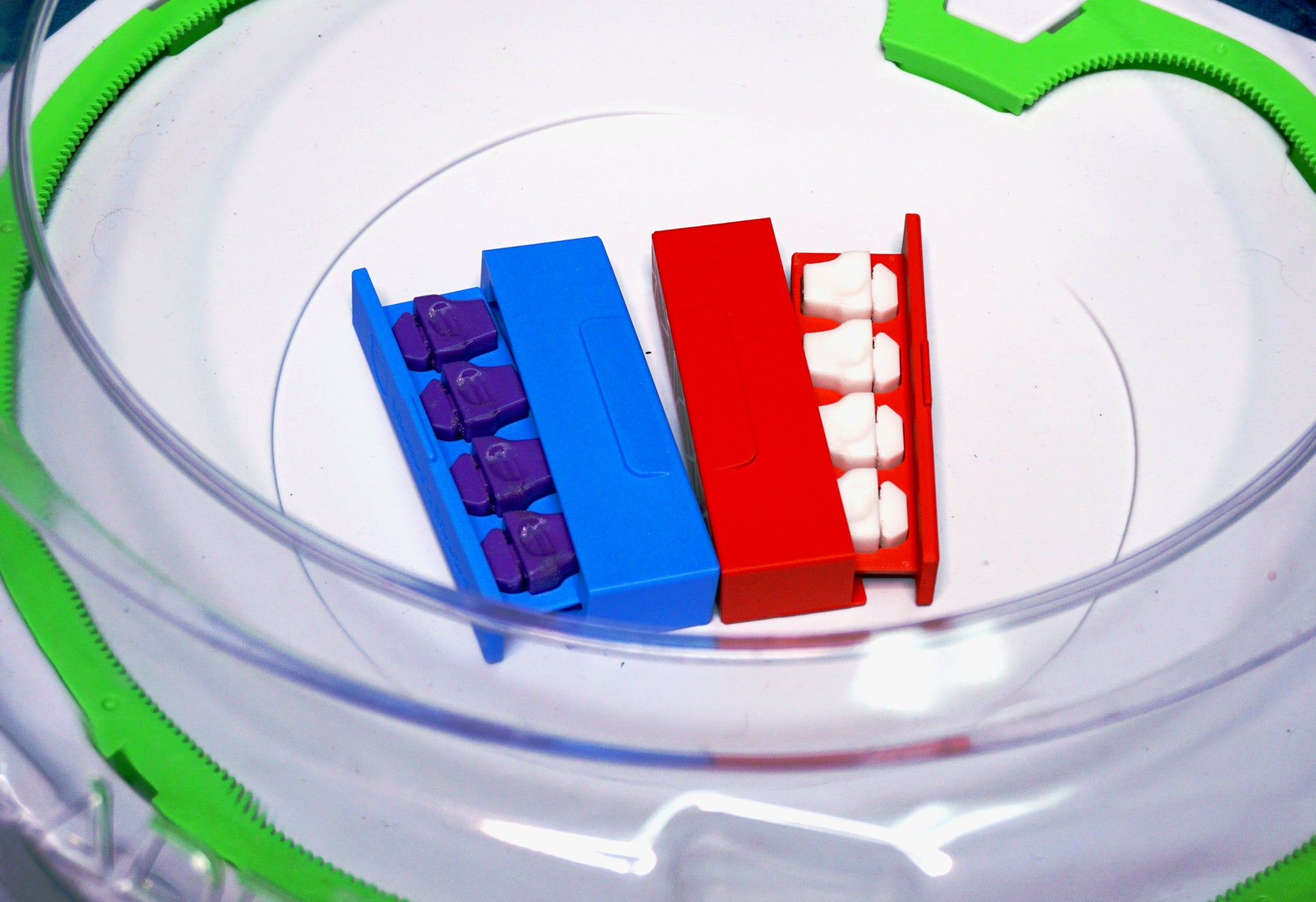 Two sets of the Stadium Level Locks in red and blue cases. The Level Locks are in Purple and White. Both sitting inside a Takara Tomy Beyblade X stadium with green X rails.