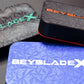Multiple of the Pocket Deck Box XL displayed on a table. The color combinations are black with green, black with red, and blue with white.