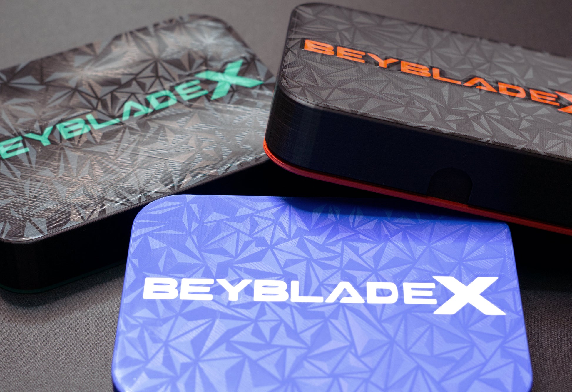 Multiple of the Pocket Deck Box XL displayed on a table. The color combinations are black with green, black with red, and blue with white.
