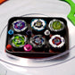 The Pocket Deck Box that holds 6 beys for Beyblade X shown in the black and red color combination. Showcasing Shark Scale, Meteor Dragoon, Wizard Rod, Emperor Pegasus Blast, Cobalt Dragoon, and Hover Wyvern. Sitting inside a Takara Tomy stadium with green and orange X-rails. 