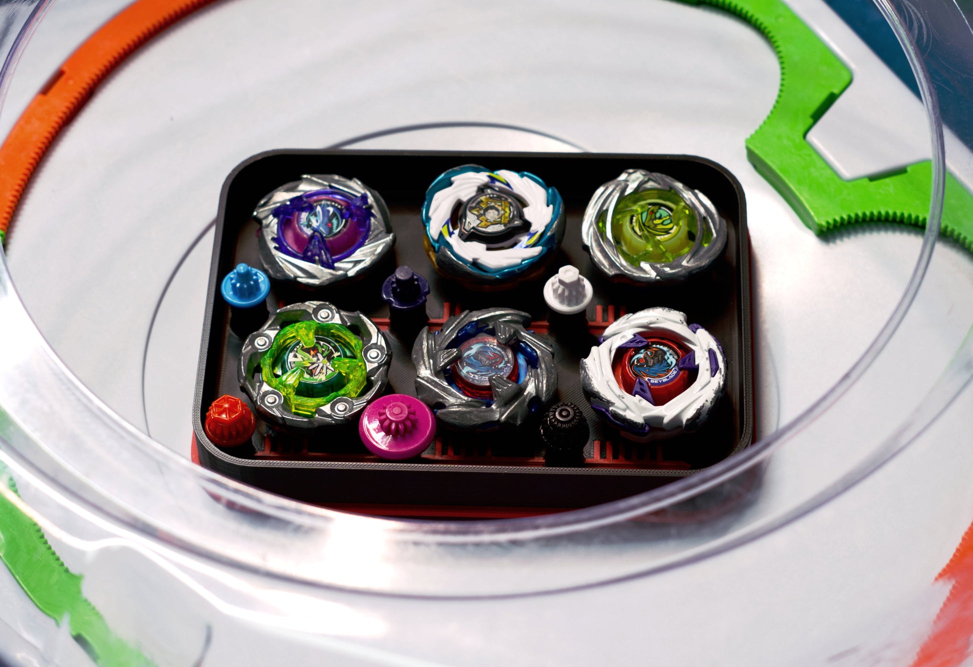 The Pocket Deck Box that holds 6 beys for Beyblade X shown in the black and red color combination. Showcasing Shark Scale, Meteor Dragoon, Wizard Rod, Emperor Pegasus Blast, Cobalt Dragoon, and Hover Wyvern. Sitting inside a Takara Tomy stadium with green and orange X-rails. 