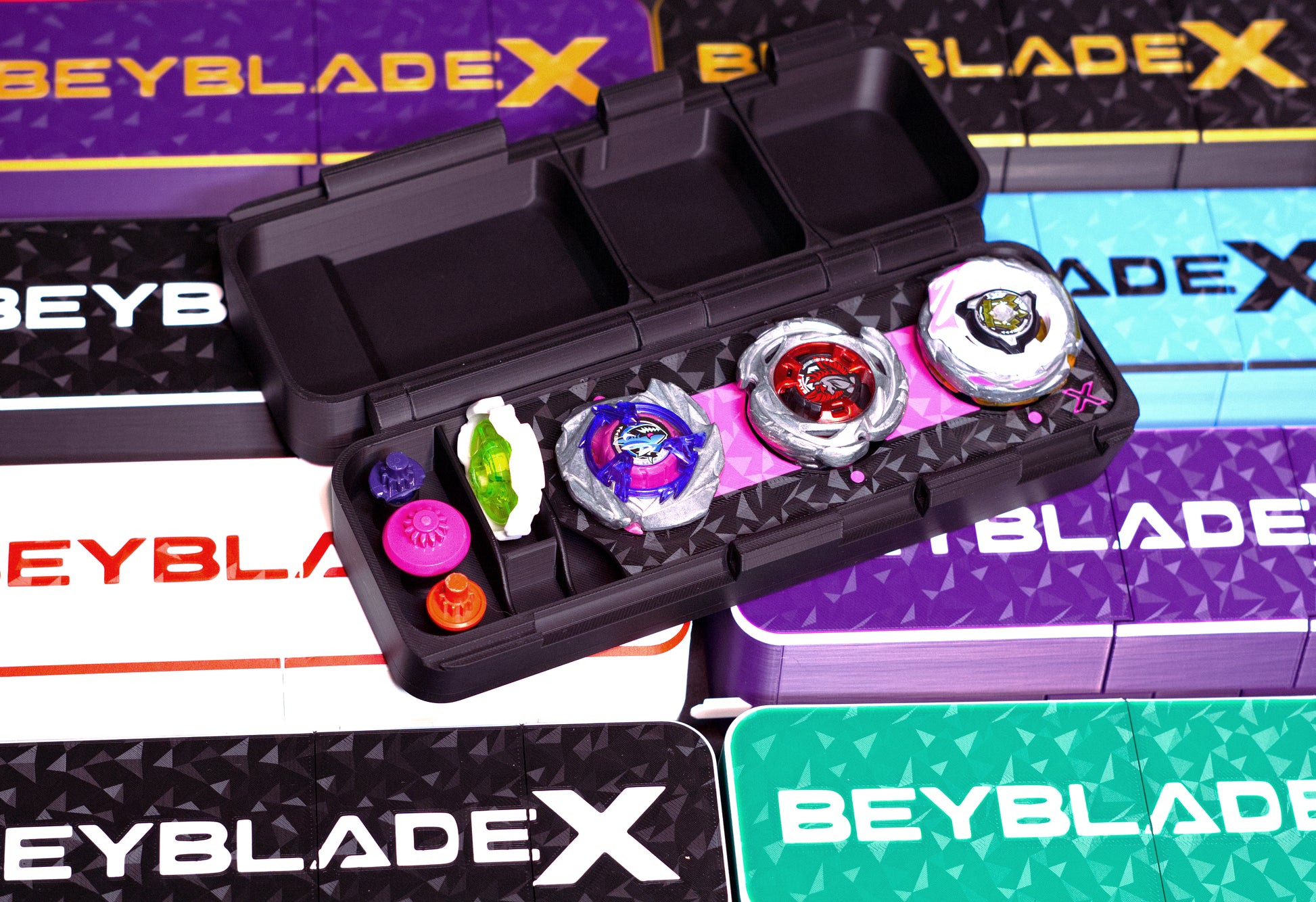 A variety of the Slam Shell EX deck boxes with one fully open showing off 3 beyblades inside it, Shark Scale, Aero Pegasus, and Delta Unicorn, with a 7-60 ratchet, and multiple its