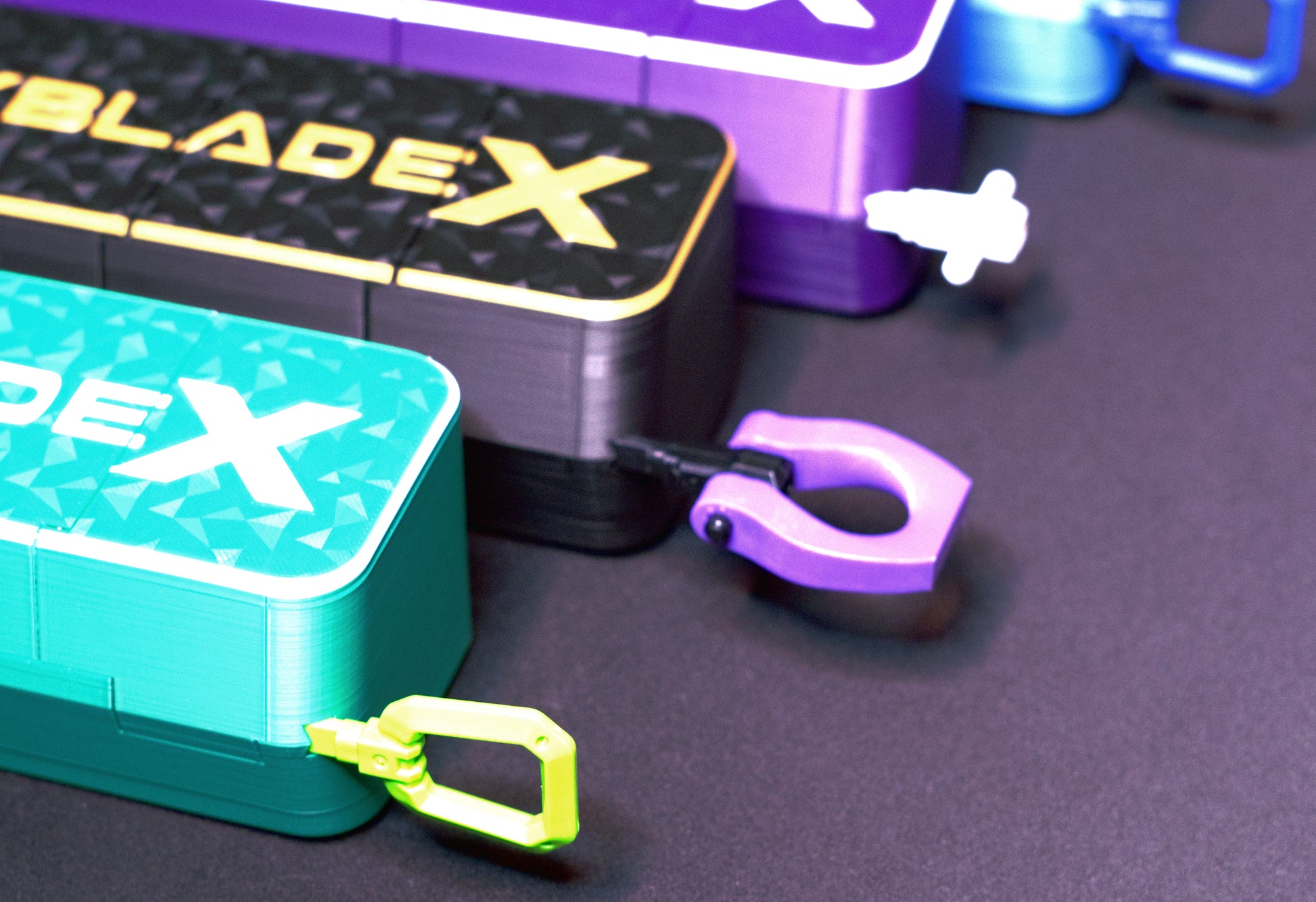 Close up shot of multiple Slam Shell EX deck boxes in a variety of colors sitting on a black table. Each with a ripcord slid through them to keep them closed