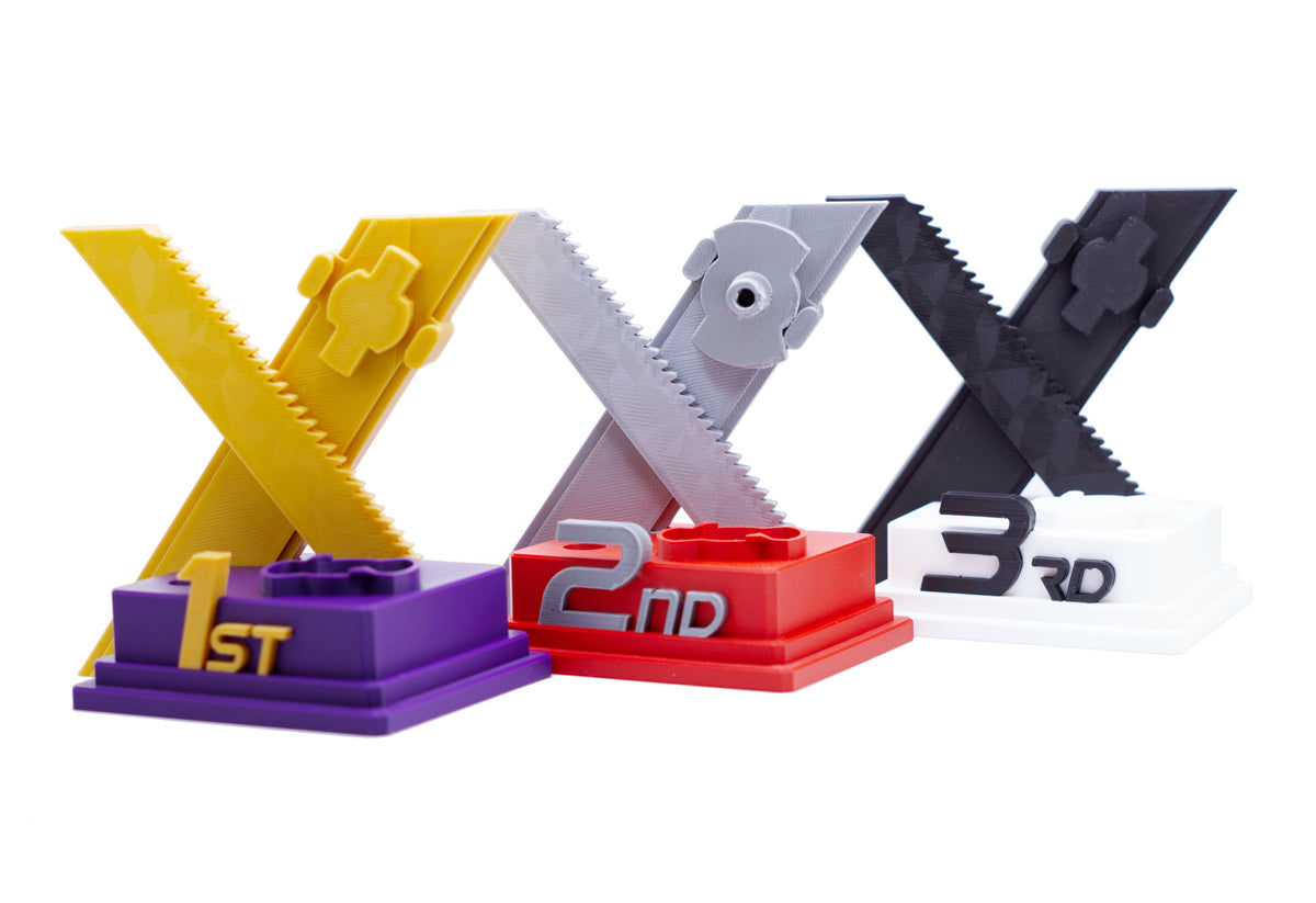 Three plastic trophy-style X-shaped stands on a white background, labeled 1st in purple, 2nd in red, and 3rd in white, with matching X-rails in gold, silver, and black.