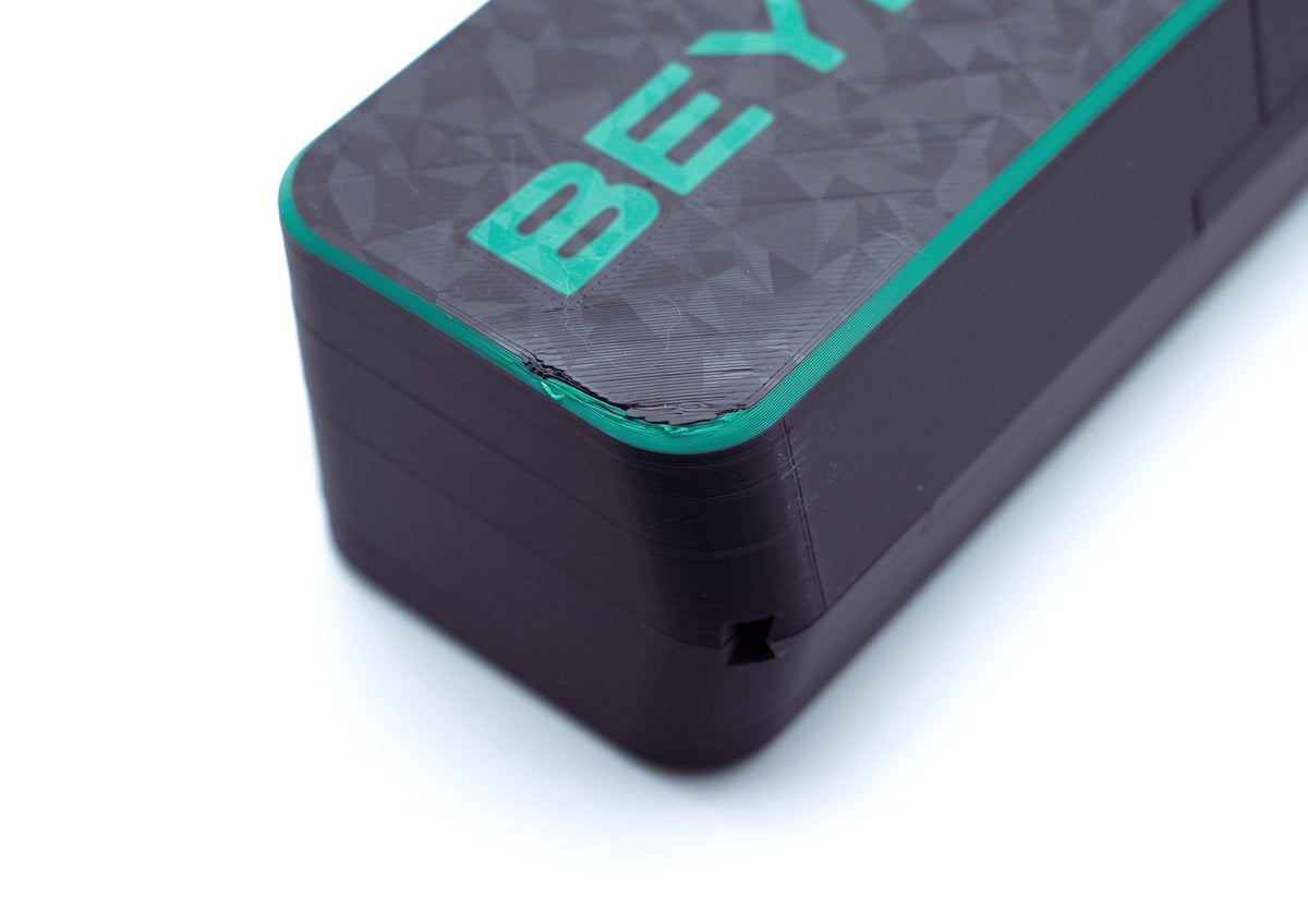 Close-up of a black rectangular electronic device with a textured top surface, featuring the partial brand name 'BEY' in bright green and a thin green accent line along the edge, set against a plain white background.