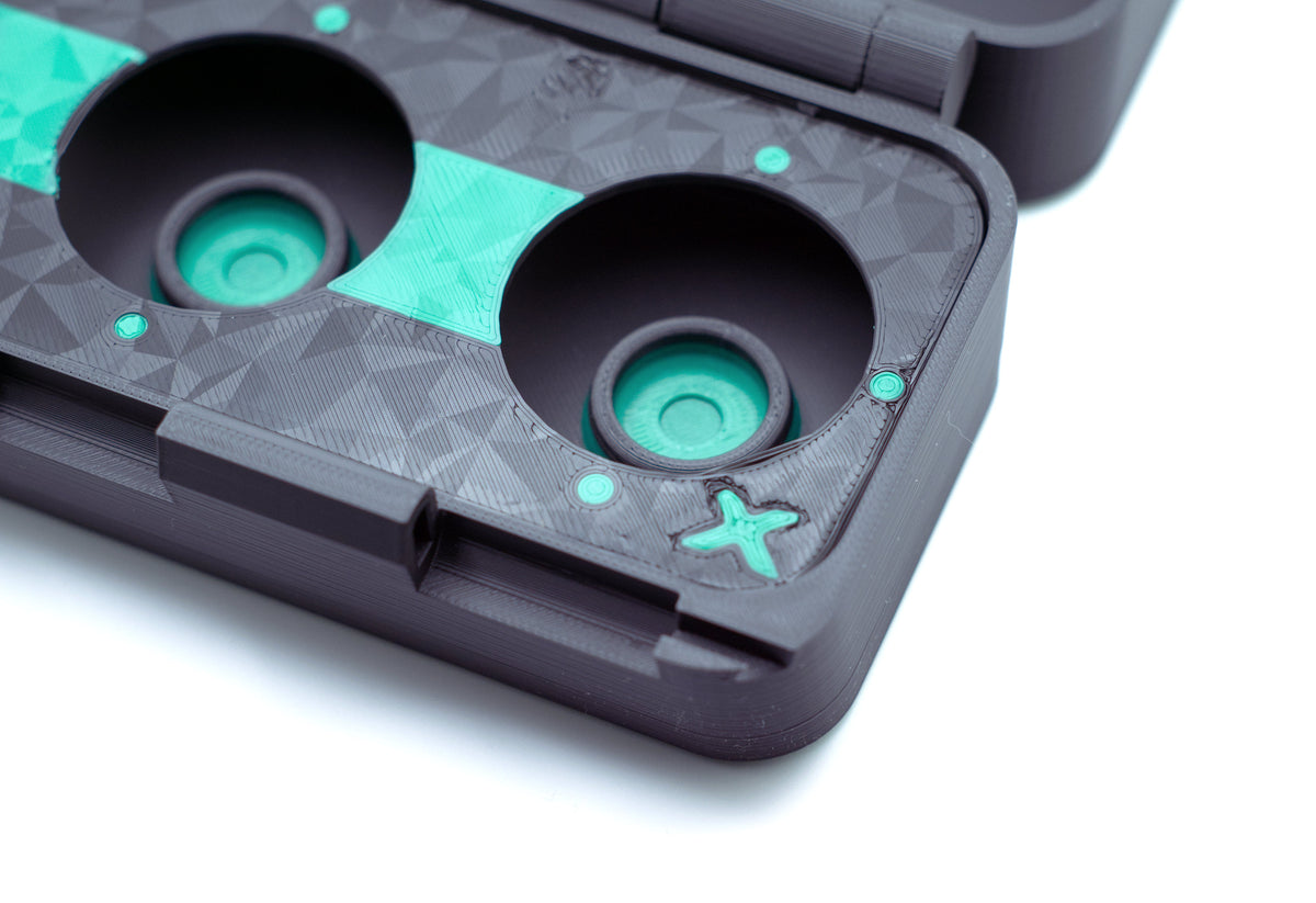 Close-up of a black 3D-printed protective case with two circular cutouts, featuring bright teal accents, a small star-shaped cutout, and a textured geometric pattern on a white background.