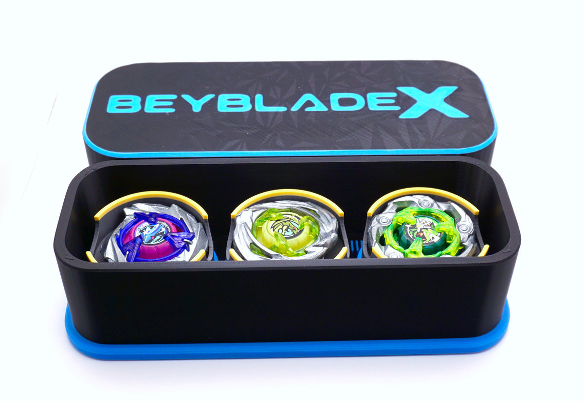 The Beyblade X Deckbox from Momo's Models shown in the black and sky blue color combination. With the lid sitting behind the base that has the Shark Scale, Hover Wyvern Pringle and Wizard Rod beyblades inside it. With everything against a white background
