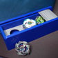 The Beyblade X Garage Door style deckbox from Momo's Models shown in blue with grey color scheme. Next to a carrying case for the Takara Tomy stadium with the Cobalt Dragoon, Pegasus Blast, and Wizard Rod beyblades.