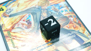 Mini Negative Dice shown in black and white with -2 on top of a Sanji alt art card from the One Piece TCG