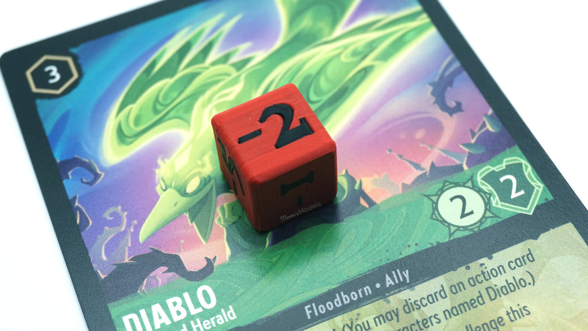 Mini Negative dice shown in red and black with a -2 on top of a Diablo card from the Lorcana TCG