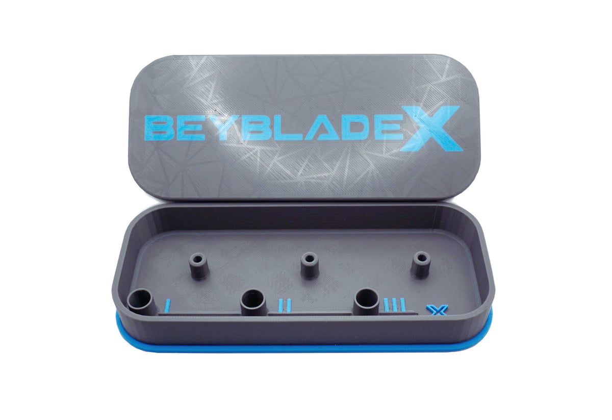 A gray rectangular case with a blue trim and the text "BEYBLADE X" in sky blue. The case is open, revealing several cylindrical holders inside. The lid has a geometric pattern.