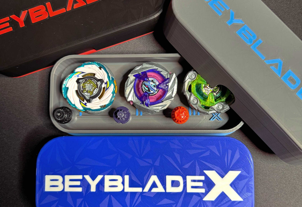 A collection of Beyblade X tops and storage cases. The tops feature various colors and designs, including green, purple, and white. The cases are black, gray, and blue, with the Beyblade X logo.
